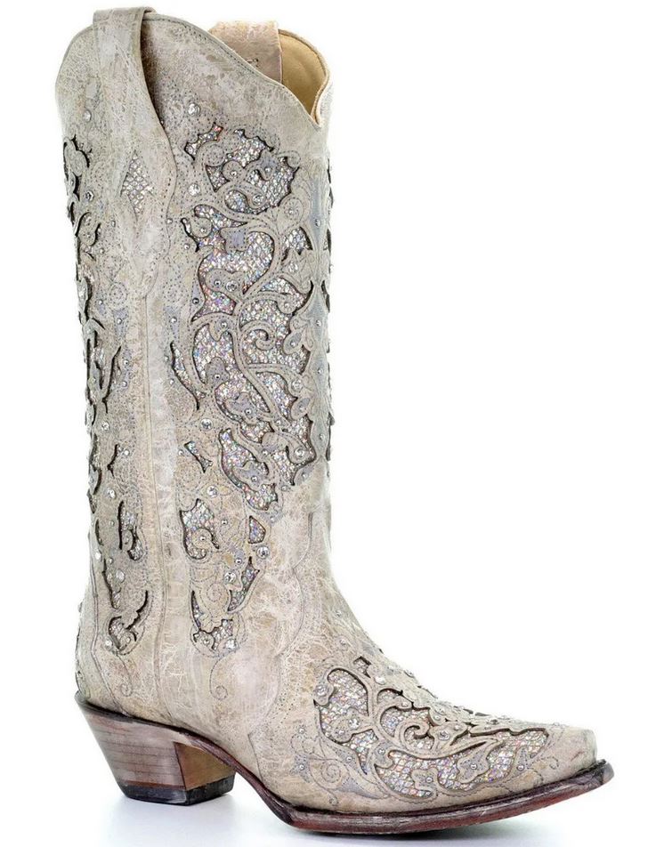 A pair of beige cowgirl boots with hollow out flower designs and rhinestone embellishments.